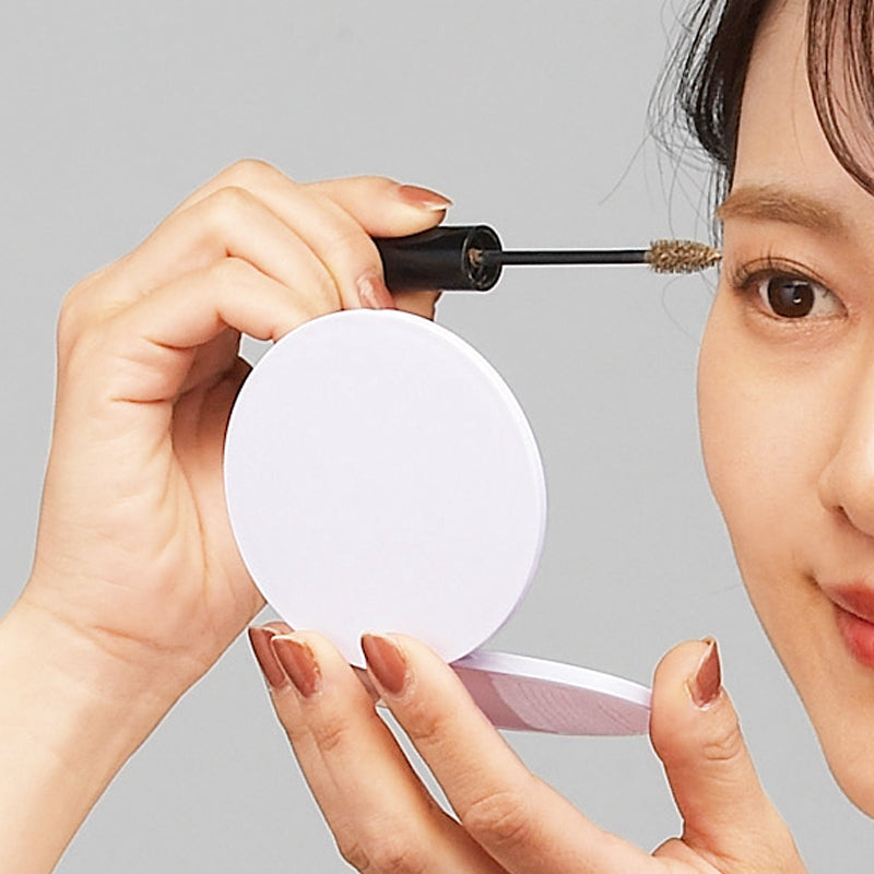 サークル ダブルコンパクトミラーを使って眉マスカラを塗っている女性